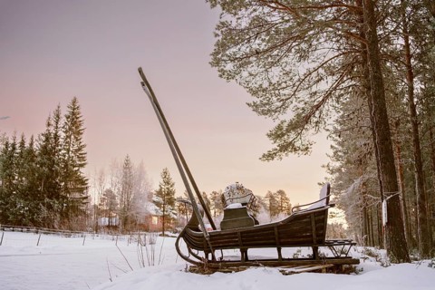 A vintage wooden sleigh rests in a serene snowy forest in Swedish Lapland at sunset. The peaceful