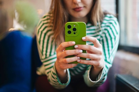 A cropped unrecognizable young woman checks her smartphone while enjoying a coffee break at a cafe.