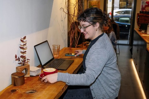 A person enjoys a latte art coffee in a cozy cafe while working on a laptop. The warm, inviting