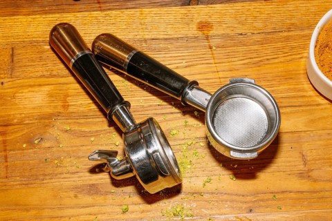 Two espresso machine portafilters rest on a wooden counter, displaying their metal baskets and