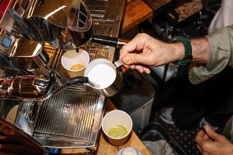 A skilled barista pours steamed milk from a metal pitcher into a cup of freshly brewed espresso,