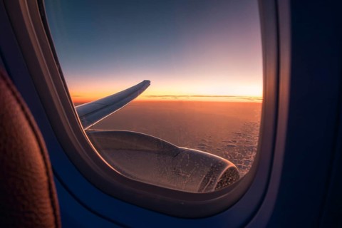 View through an airplane window catching the glowing sunset skyline above the clouds, with the