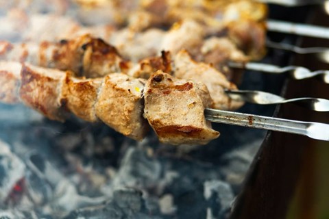 Close-up of juicy, chunky kebabs sizzling on skewers over a smoky grill at a bustling street fair,