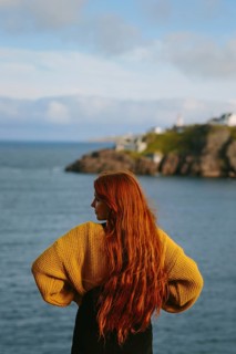 Back view of an unrecognizable woman with long red hair, standing at Cape Spear Lighthouse,