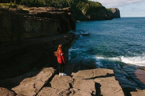 Back view of a young unrecognizable redhead woman standing on the rocky shoreline of Flatrock,