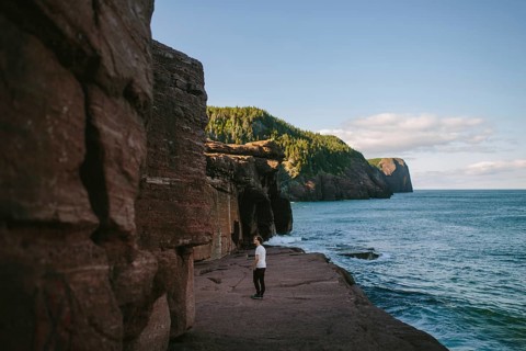 A young man standing on a rocky cliff overlooking the ocean at Flatrock, Newfoundland and Labrador,