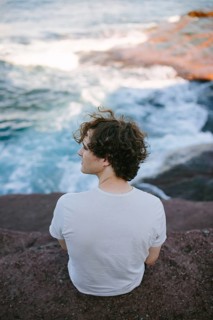 Back view of a young man at Flatrock looking out at the turbulent ocean waves and rocky coastline,