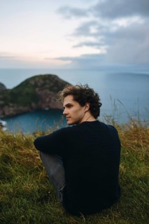 A young male sits serenely overlooking the calm waters from Signal Hill, St. John's. His relaxed