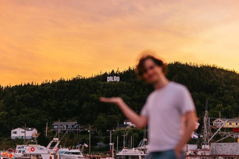 A young blurred Caucasian man playfully gestures towards the town sign DILDO in Dildo, Newfoundland