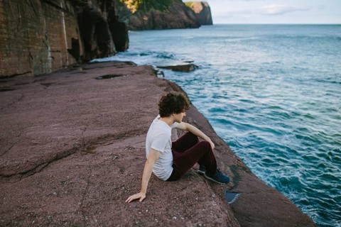 A young male sits contemplatively by the serene sea at Flatrock, Newfoundland, enjoying a tranquil