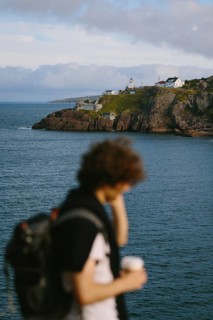 Unrecognizable man with curly hair, sipping coffee while overlooking the rugged coastline and the