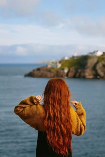 Back view of unrecognizable woman with long red hair, wearing a yellow sweater, overlooking a