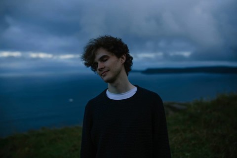 A thoughtful young man with eyes closed stands by the ocean in Signal Hill in St. John's,