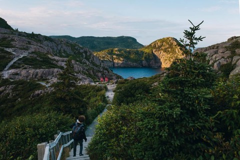 Back view of an unrecognizable hiker walking a wooden pathway towards a picturesque bay surrounded
