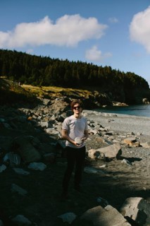 A young man stands on the rocky shores of Middle Cove in Newfoundland & Labrador, Canada. He is
