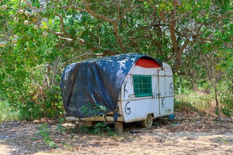 An old caravan with black cover stands in a rustic landscape under trees, Pantanal, Mato Grosso,