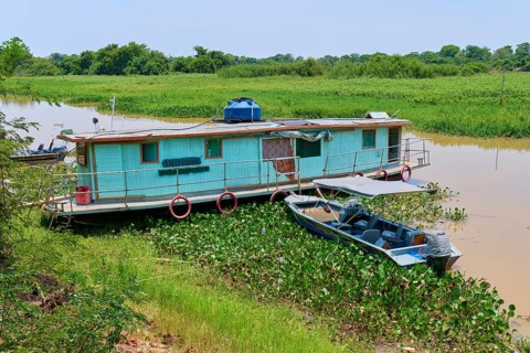 A houseboat parks on the riverbank next to a small boat surrounded by aquatic plants, Porto Jofre,
