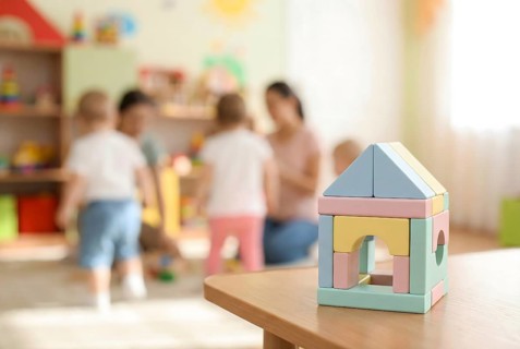 Pastel wooden building bricks toys and blurry playing children in background in children day care