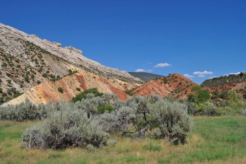 Rocks with colorful soil, vegetation and blue sky in hilly landscape, Dinosaur National Monument,