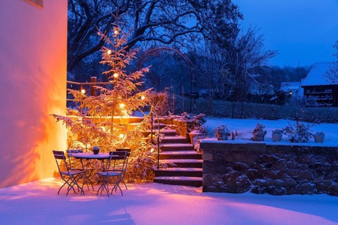 Still life with illuminated Christmas tree, stairs and table with chairs in the snow at blue hour,