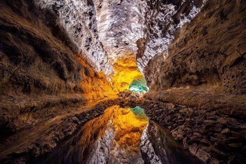 Lava tunnel, illuminated lava cave with perfect reflection in an underground lake, Cueva de los