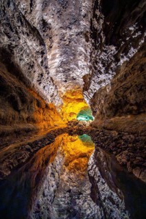 Lava tunnel, illuminated lava cave with perfect reflection in an underground lake, Cueva de los