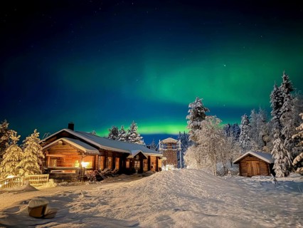 Northern lights, aurora borealis in the night sky, illuminated wooden house in snowy landscape,