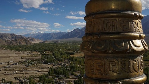 View from a monastery across the valley a golden prayer wheel in the foreground with a vast