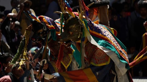 People wearing colorful masks and costumes conduct an outdoor ceremony, traditional cultural