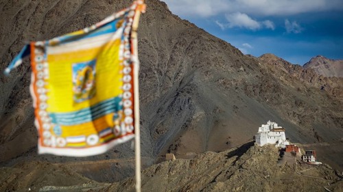 View of Namgyal Tsemo Buddhist mountain temple, with colorful prayer flags against a blue sky,