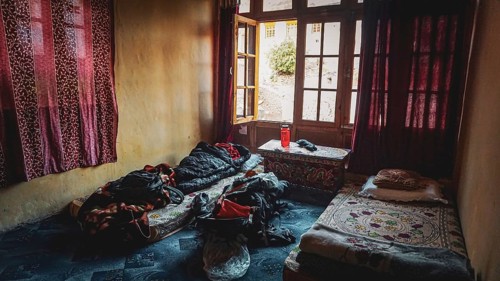 A simple room in a mountain village in the Indian Himalayas with two beds, backpack and cinder and