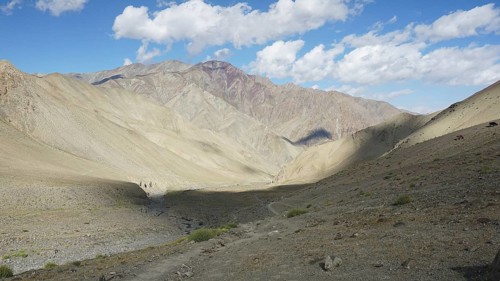 Wide mountain valley under a partly cloudy sky with a small path, trekking in Ladakh, Stok la,