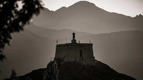 A monastery is majestically perched on a hill with mountains in the background at dusk, Leh,