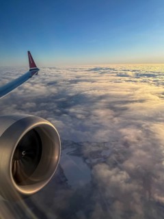 Airplane wing over sea of clouds in morning light, aerial view, Finland