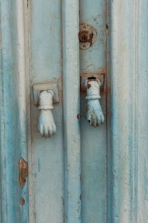 Old decorative hand shaped door knockers on a traditional blue painted door on an house in the