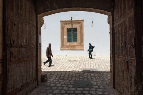 Tunisian men and women walk past some old wooden doors beside Bab Diwan the gate to Sfax Medina,