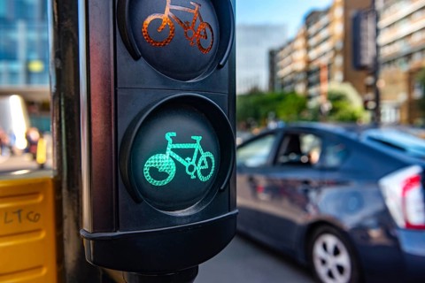A green cycle lane traffic signal at a junction in a busy London city street with a car passing in