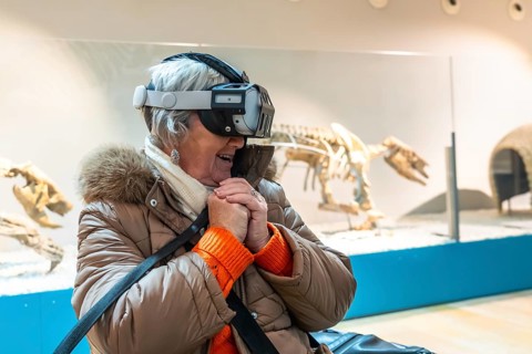 Senior woman wearing a vr headset, smiling with hands clasped while immersed in an interactive