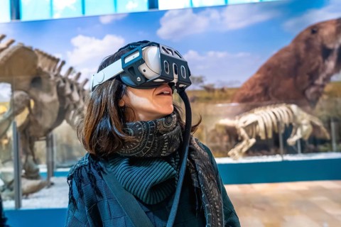 Woman experiencing virtual reality with a headset on, exploring ancient animals and paleontology in