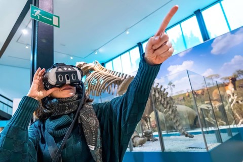 Woman wearing a virtual reality headset and pointing upward, interacting with an immersive