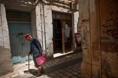 An old Tunisian man wearing a traditional red Chechia walks in the narrow alleyways of Sfax Medina,