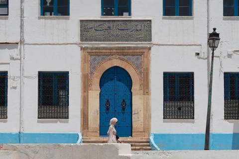 A Tunisian woman walks past the beautiful blue ornate door and architecture of the Abbasid School