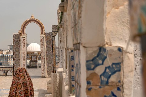 A rooftop view of a domed building through an archway decorated with traditional mosaic designs,