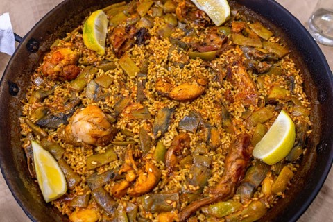Traditional valencian paella cooking in a large pan with rice, chicken, rabbit, lima and green