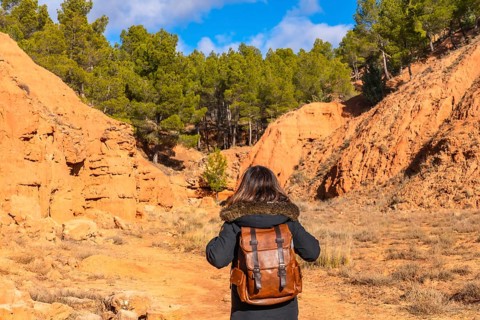 Hiker with a brown backpack walking through the unique red clay terrain of las arcillas natural