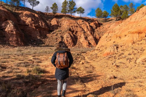Woman backpacker exploring desert landscape with unique red clay formations and pine trees under a