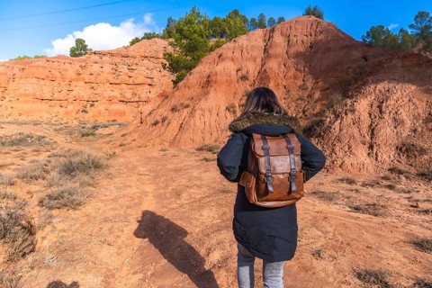 Woman with brown leather backpack and warm coat walking a dirt trail through las arcillas natural