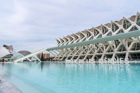The museu de les ciencies principle building stands prominently against a cloudy sky, reflecting in