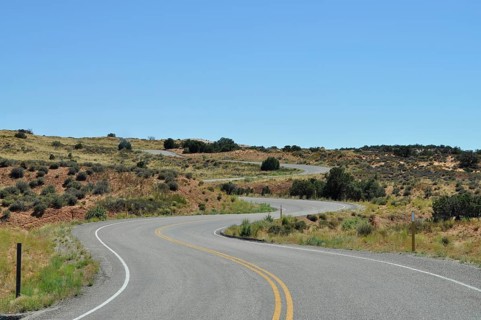 Winding road through a slightly hilly, dry desert landscape under clear skies, Canyonlands National