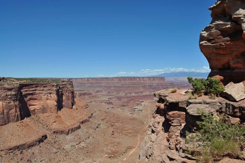 Rock cliffs with spectacular views of the vast, dry desert landscape and a narrow gravel road,